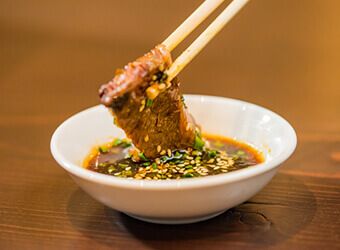 「さつま」秘伝のタレにお肉をつけているイメージ